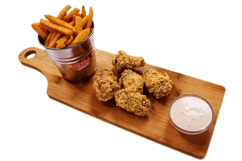 Crispy fried chicken bites with seasoned fries and dipping sauce on a wooden board